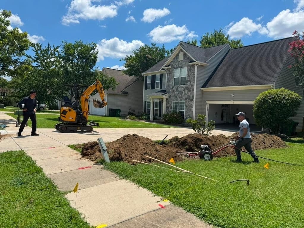 Residential driveway excavation in progress with yellow machinery and workers on a sunny day