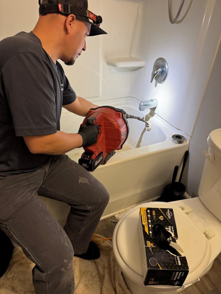 Plumber in black cap and gloves working on bathtub drain with pipe wrench and tools